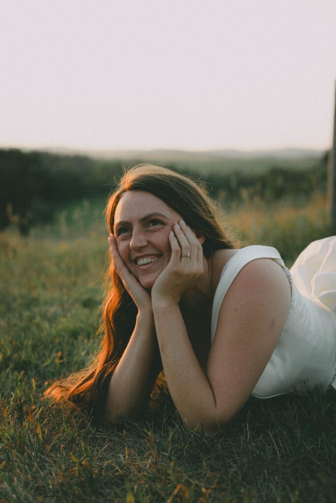 Bride laying on the ground cupping her face looking up during sunset