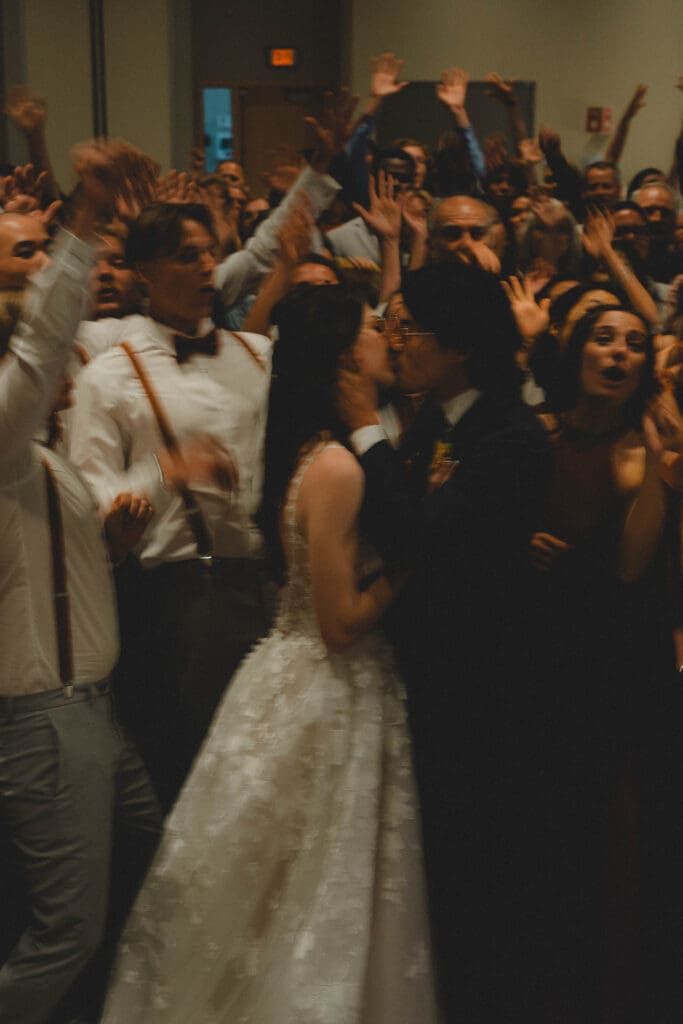 Wedding couple kissing with a crowd behind them cheering