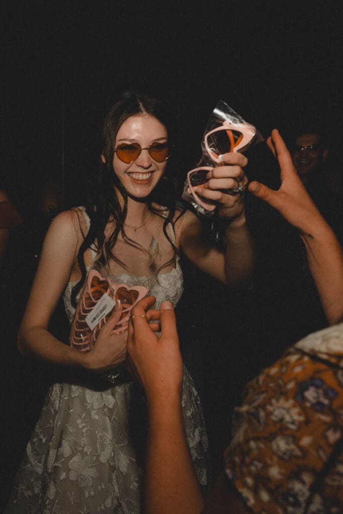 Bride laughing and hanging out heart shapes glasses at her wedding dance