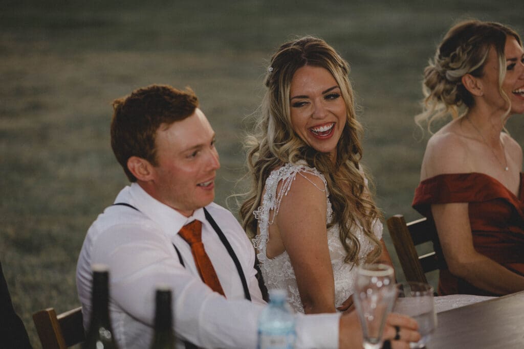 Bride laughing and looking at the Groom while they sit at the head table during a reception 