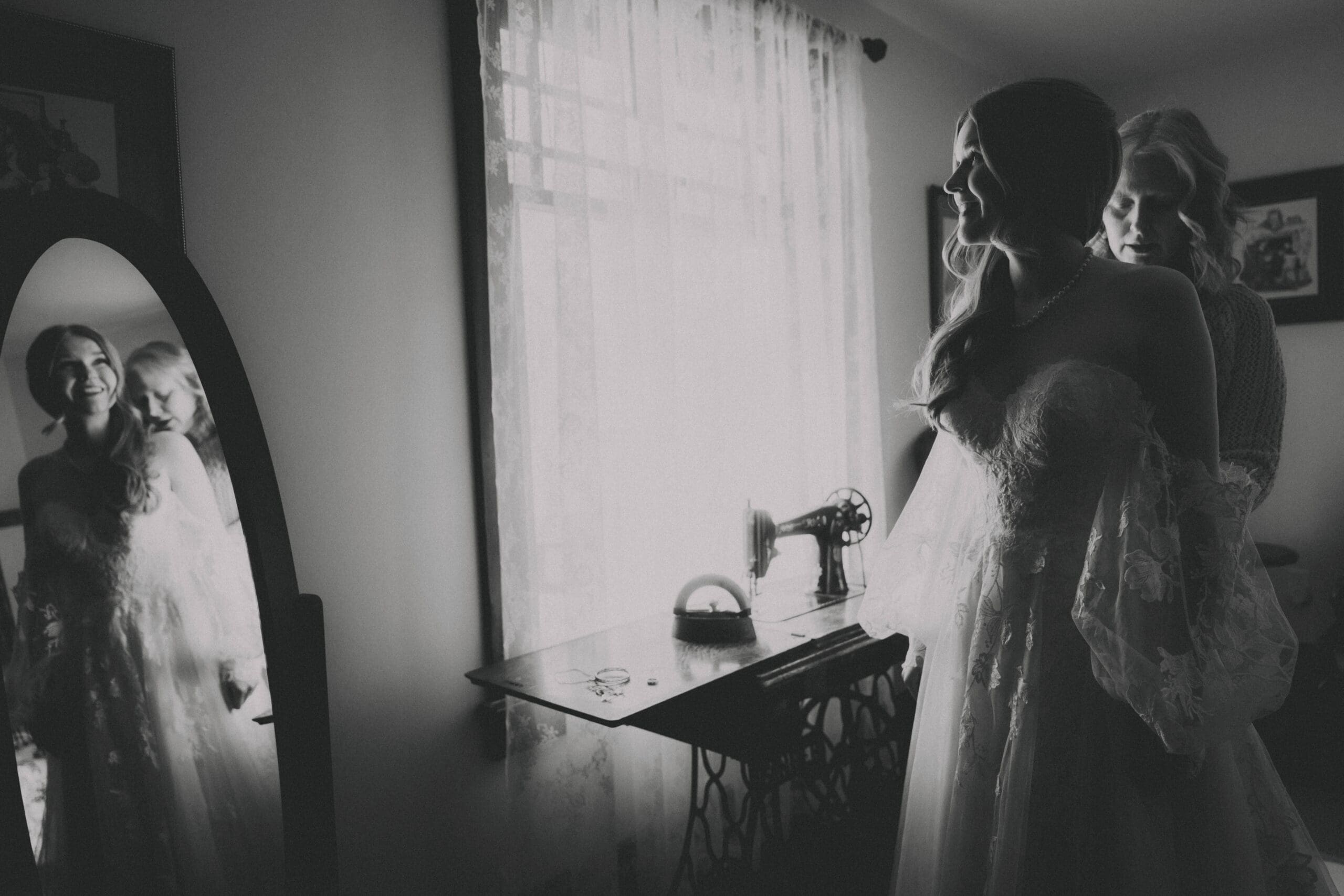 Bride looking in a mirror as her Mom buttons up the back of her dress